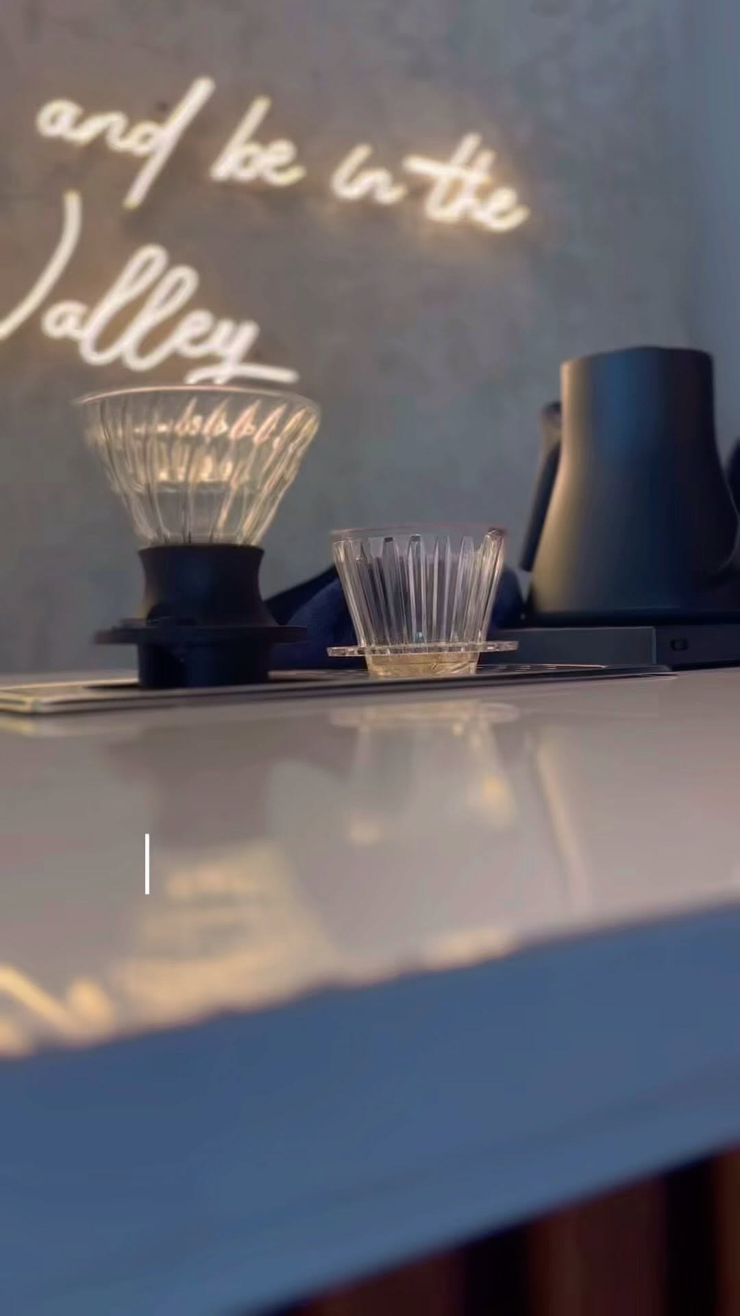 Happy Valley Café bar counter — neon 'Valley' cursive sign glowing above the pour-over station at night